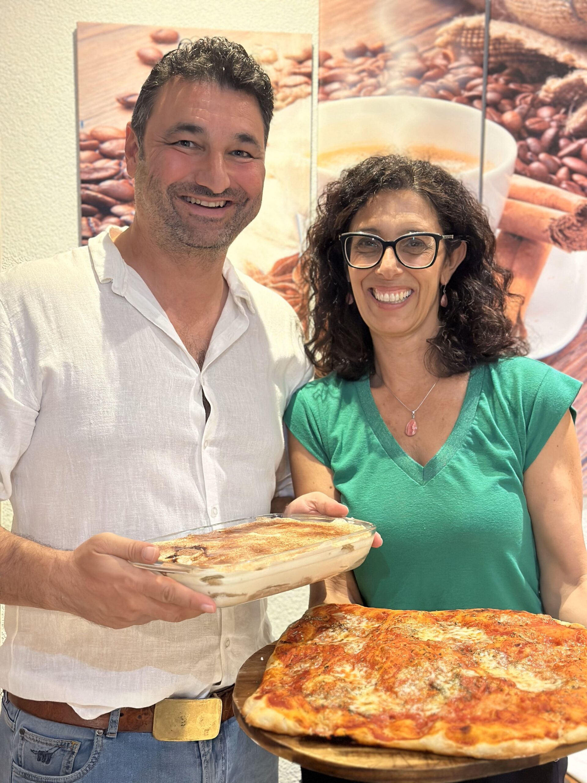 Es lächelnds Paar, wo e selbstgmachti Pizza und es Dessert i de Händ hält.