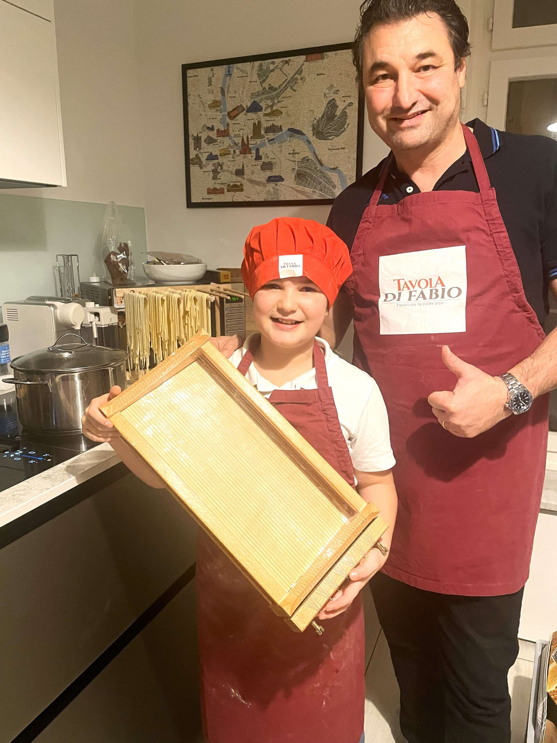 Kinder in Kochschürzen präsentieren stolz selbstgemachte bunte Pasta während eines Kinder-Kochkurses.